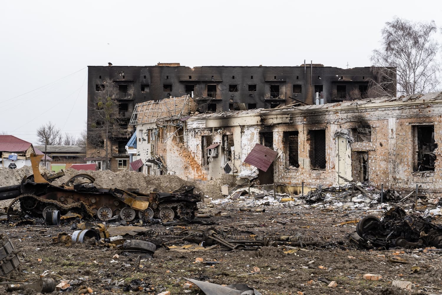 Остов сгоревшей бронетехники на фоне разрушенных и обугленных зданий.