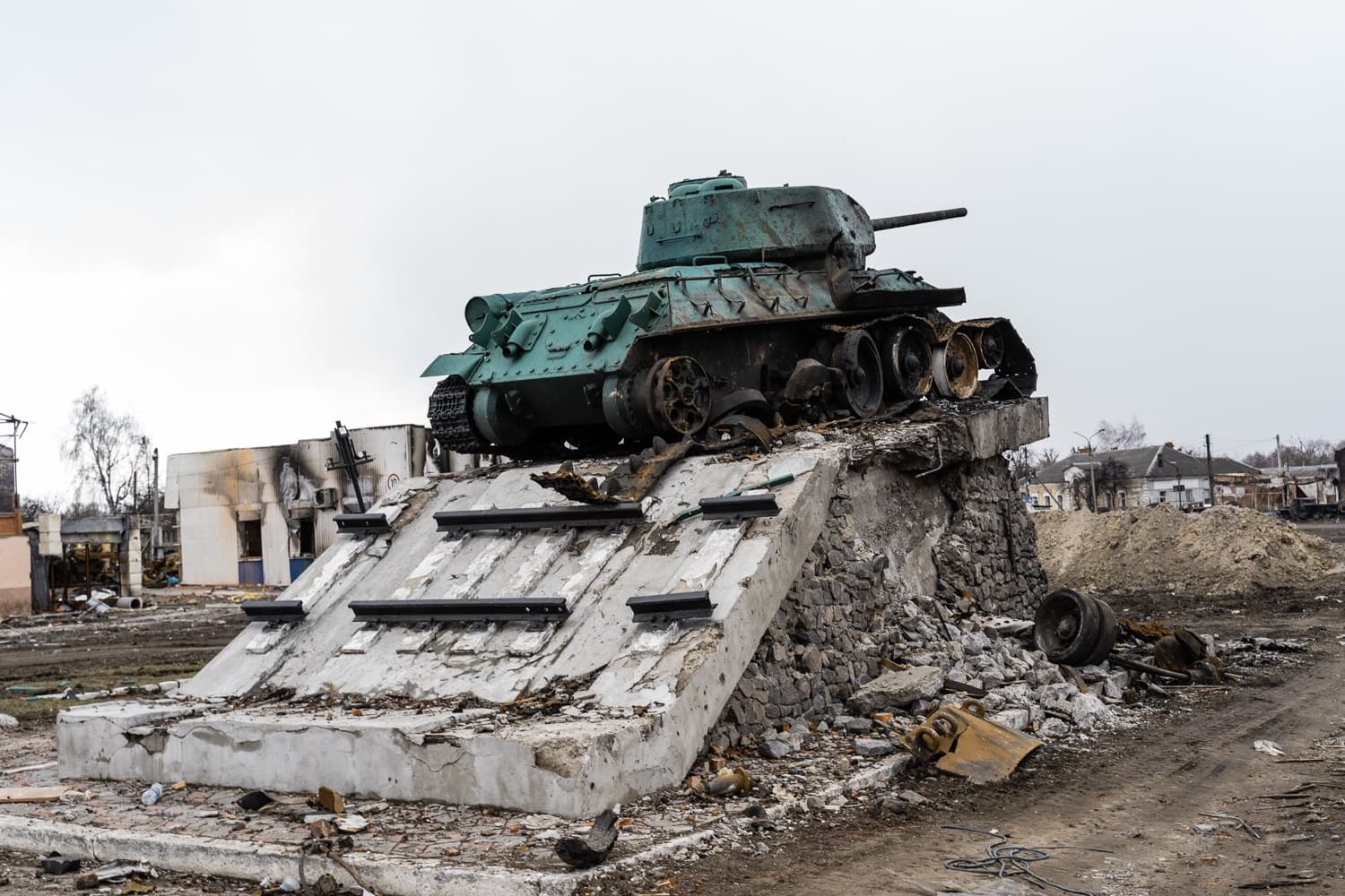 Зеленый танк-памятник Т-34 на разрушенном бетонном постаменте среди руин.