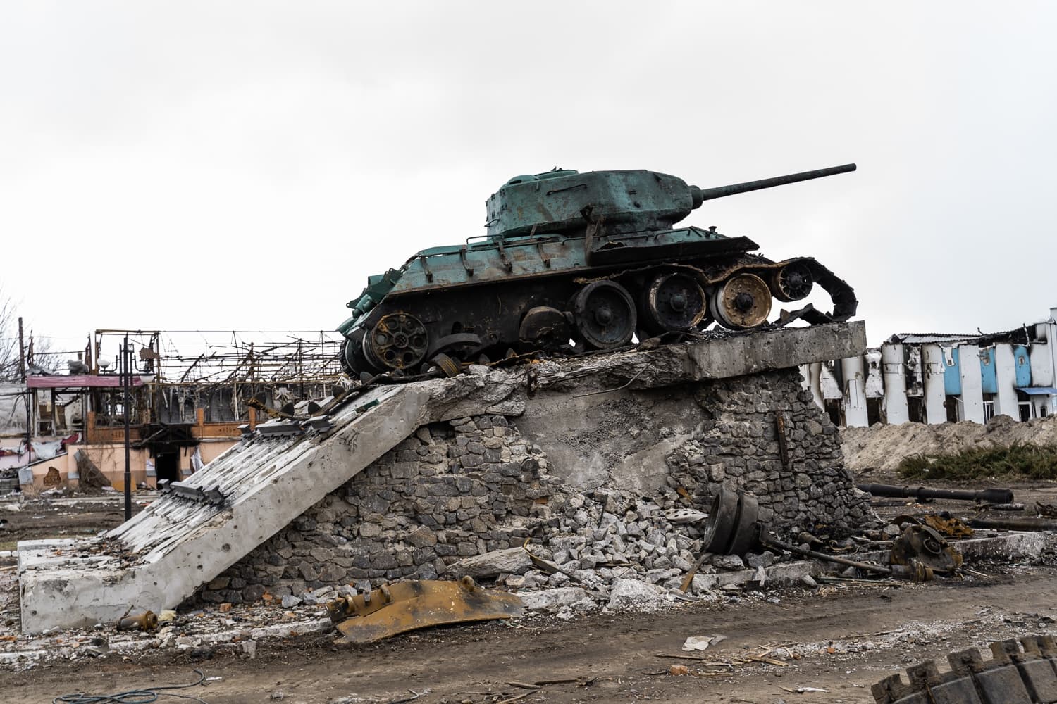 Обгоревший танк Т-34 на разрушенном каменном постаменте, на фоне руин зданий.