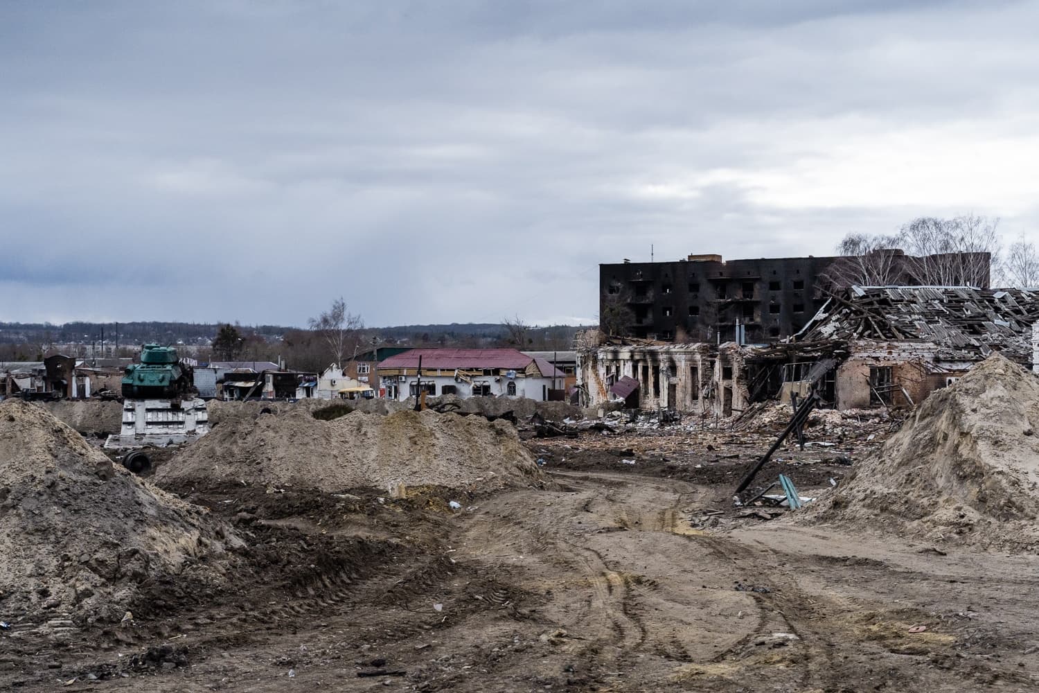 Разрушенный город: сгоревшие многоэтажные и руины домов на фоне грязного поля, виден танк-памятник.