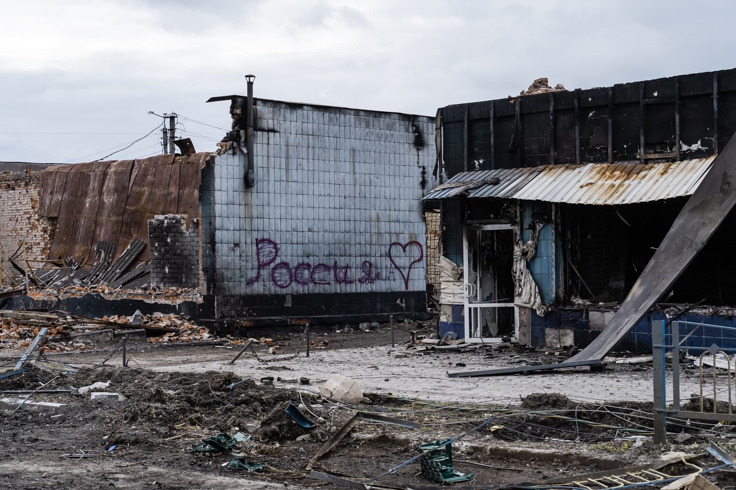 Руины разрушенных и обгоревших зданий с разбросанным мусором. На уцелевшей стене граффити "Россия ❤️".
