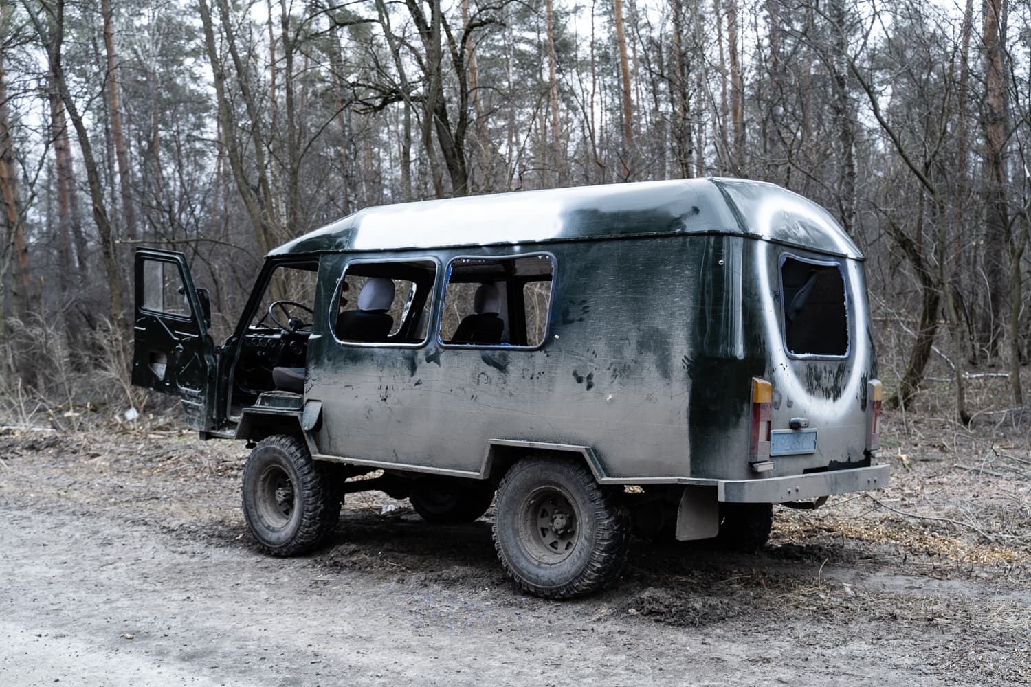 Грязный, сильно модифицированный внедорожник-фургон (зеленый с белым верхом) с открытой дверью на лесной грунтовой дороге.