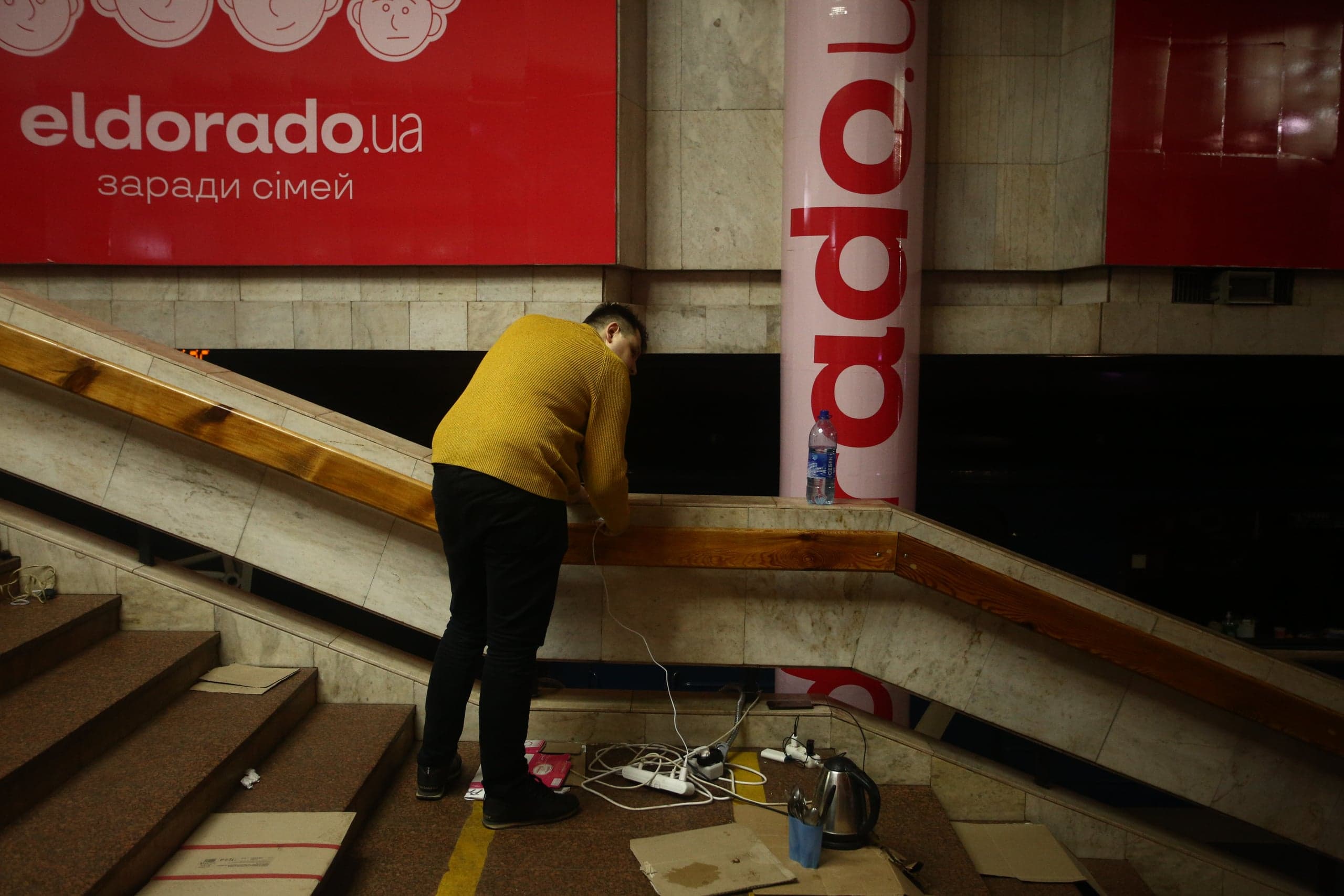 Мужчина в желтом свитере у лестницы метро с удлинителями и чайником. Реклама: "eldorado.ua заради сімей".