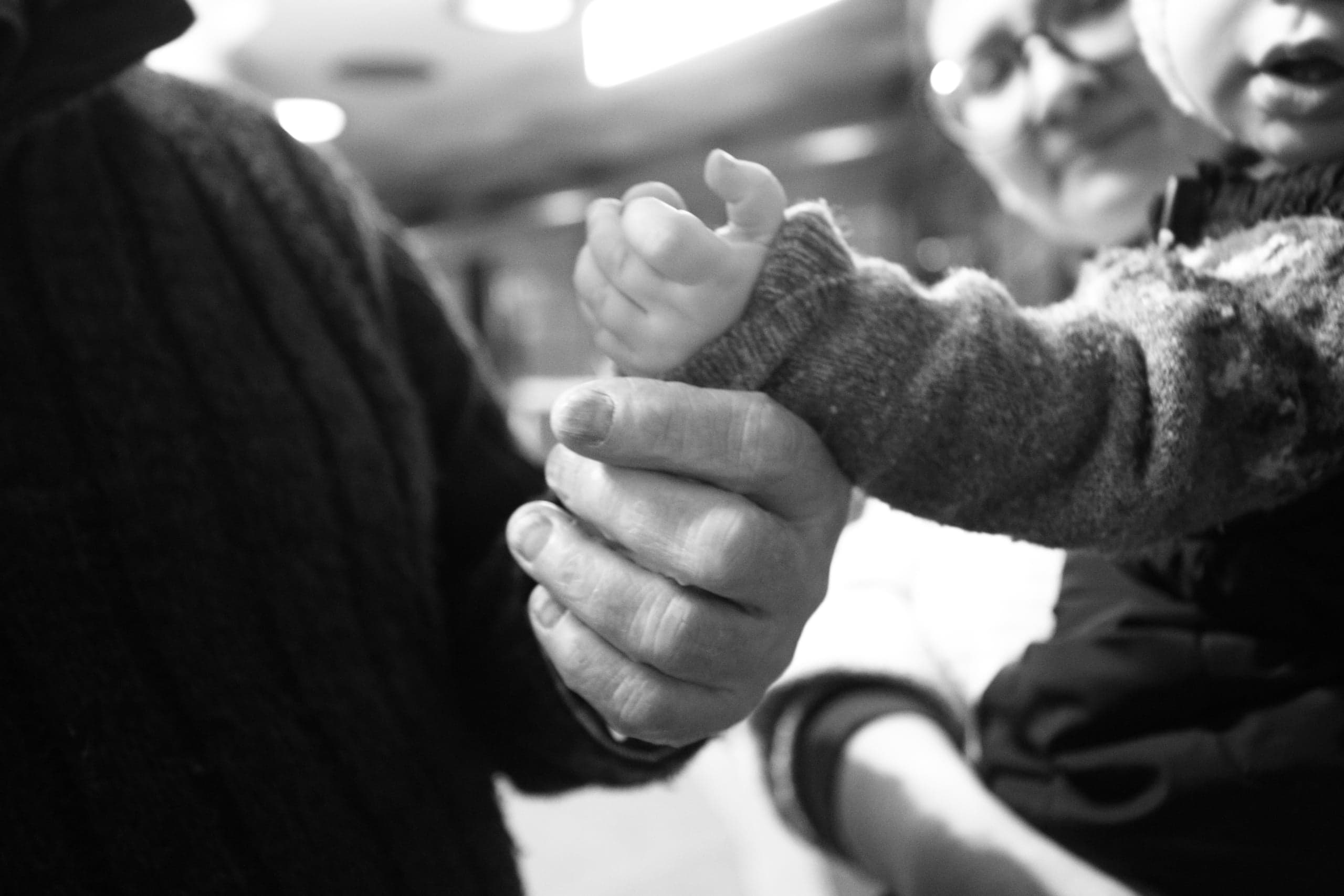 Черно-белый крупный план: взрослая рука держит маленькую руку ребенка в вязаном рукаве.