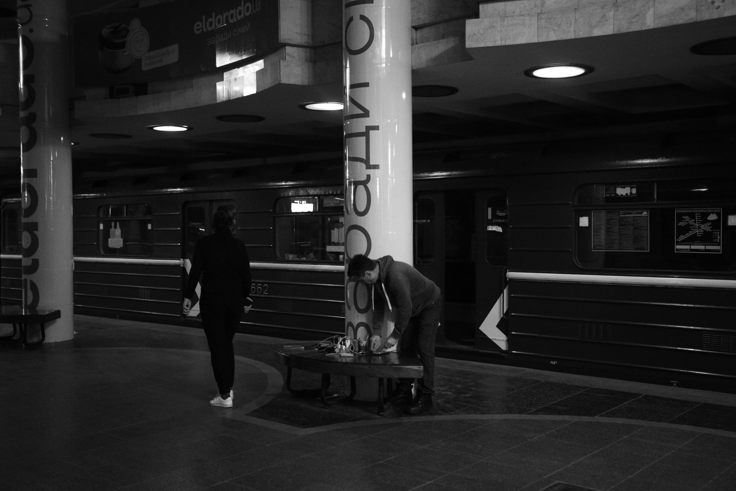 Контрастный ч/б снимок станции метро. Мужчина склонился над скамейкой у колонны с надписью "радио С". На фоне темный вагон поезда с номером "662".