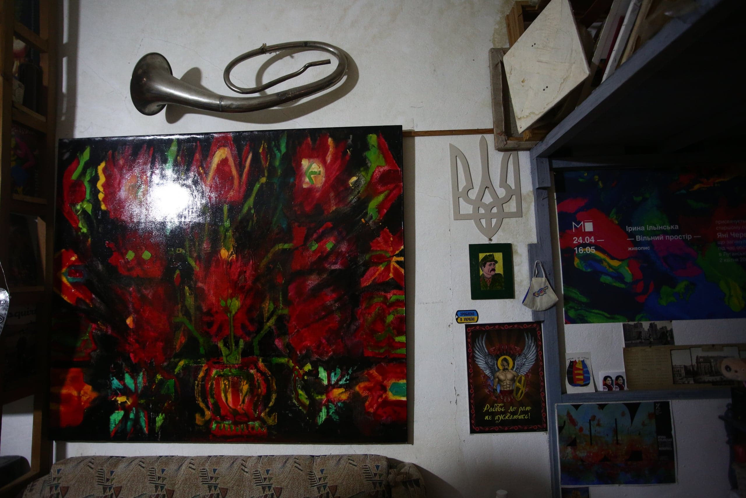 Студийный интерьер. На стене: большое абстрактное полотно с красными цветами, металлический горн, деревянный Тризуб и постер с текстом: "Радій, де рано чи пізно не мусiшся!".