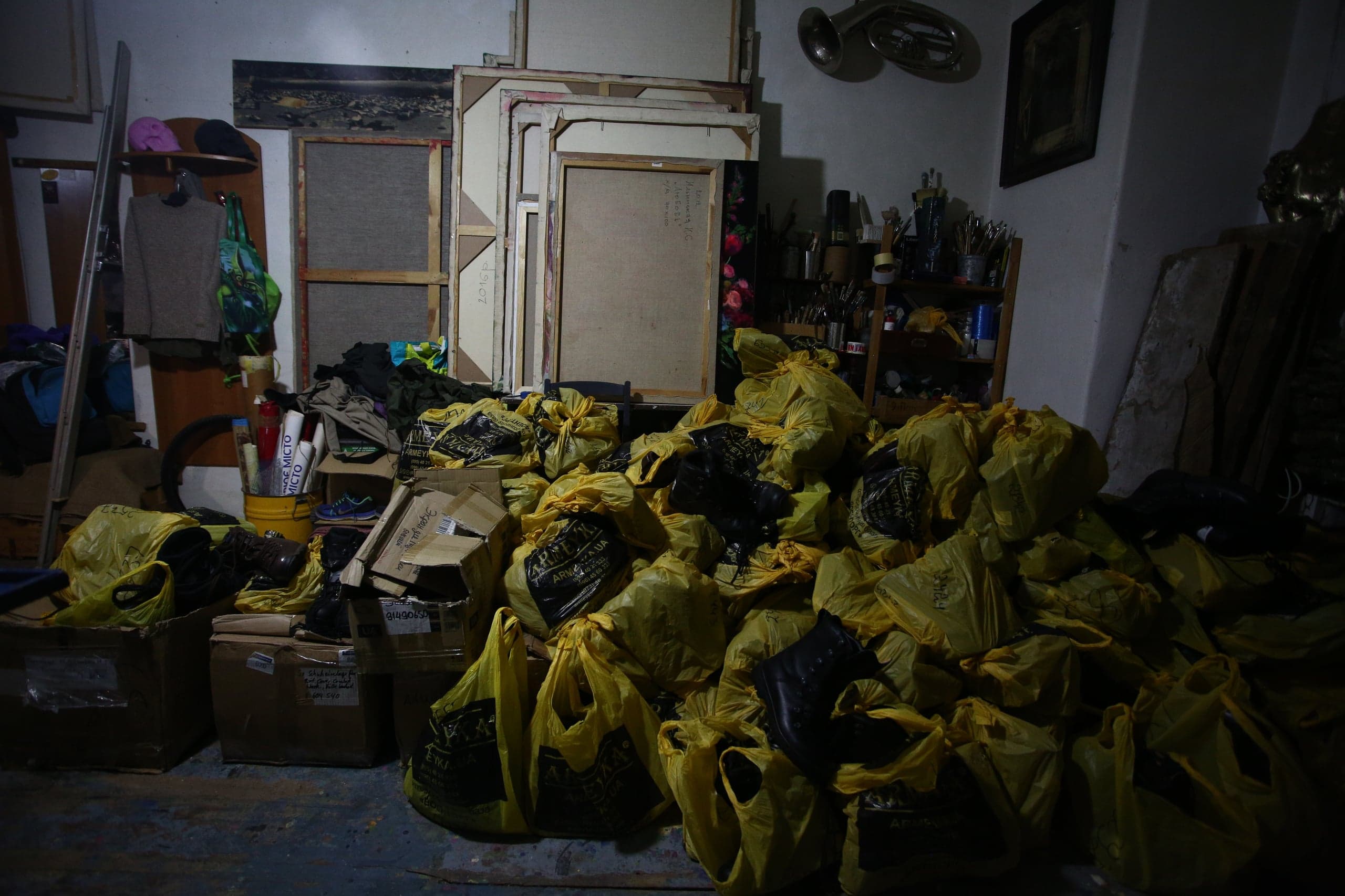 Захламленное помещение; груда желтых пакетов на полу. На заднем плане стопки холстов, принадлежности для рисования, картонные коробки и туба на стене. На рулоне текст "МІСТО".