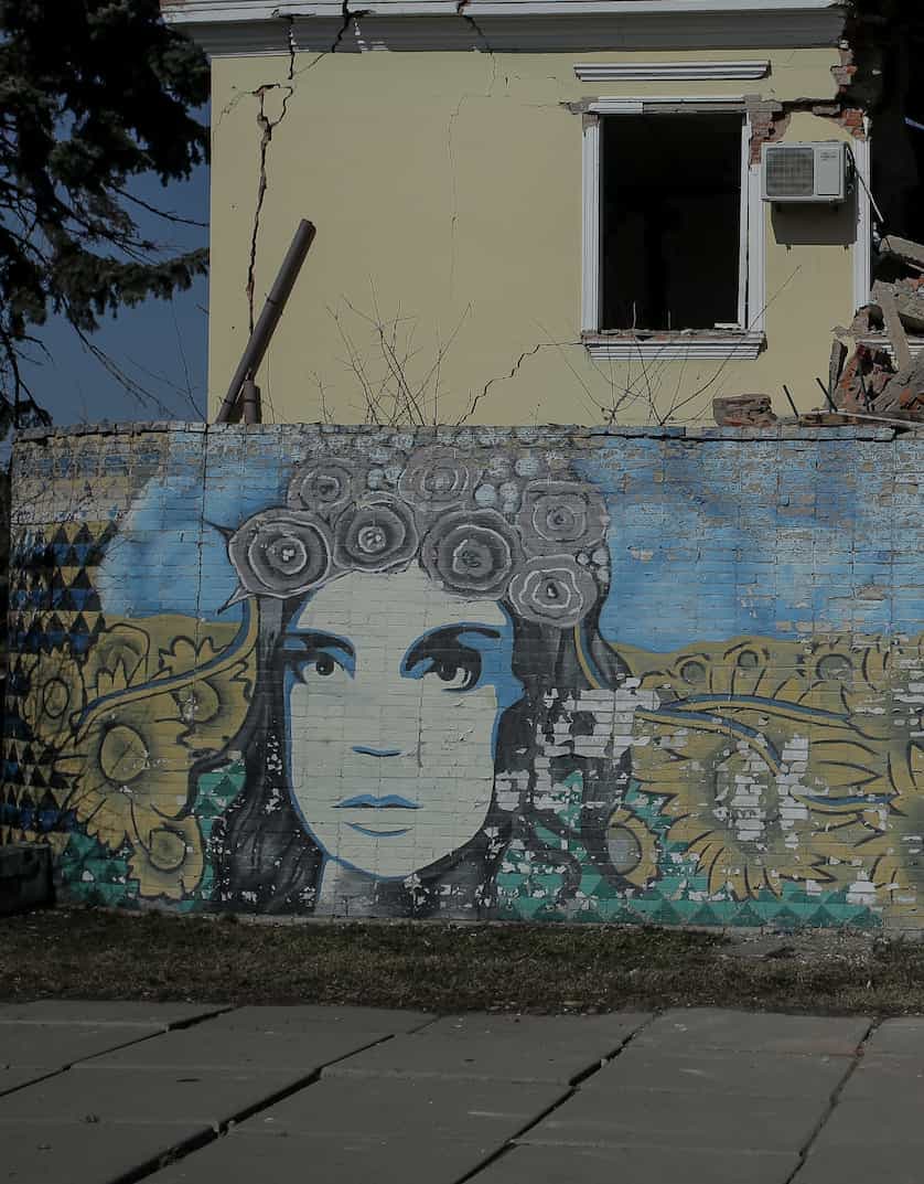 Graffiti on the wall of a destroyed building depicting a woman's face framed by sunflowers.