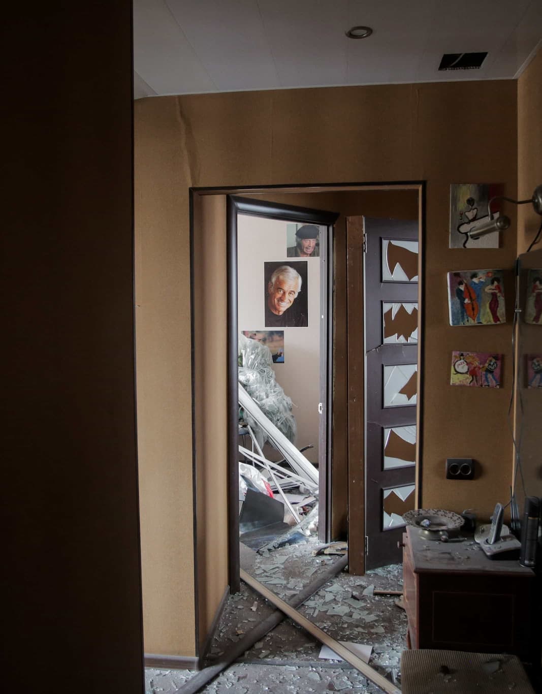 A destroyed residential room, debris on the floor, a damaged door and interior are visible.