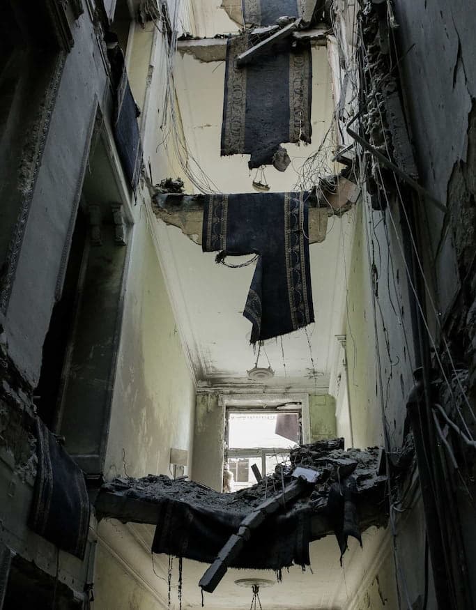 Destroyed building showing all three floors, with carpets hanging from the holes in the floor.
