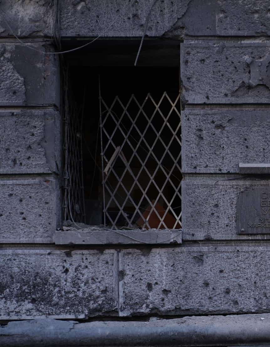 A barred window in a dark, dilapidated building with stone masonry.