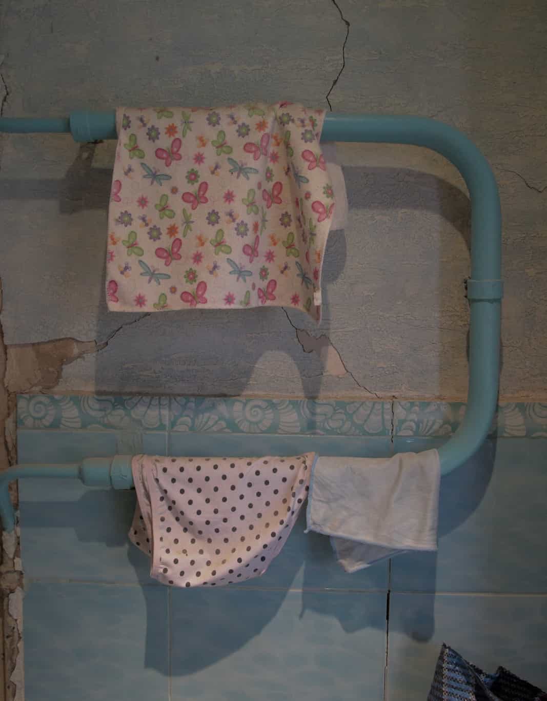 Towels and underwear drying on a pipe against the backdrop of a cracked wall.